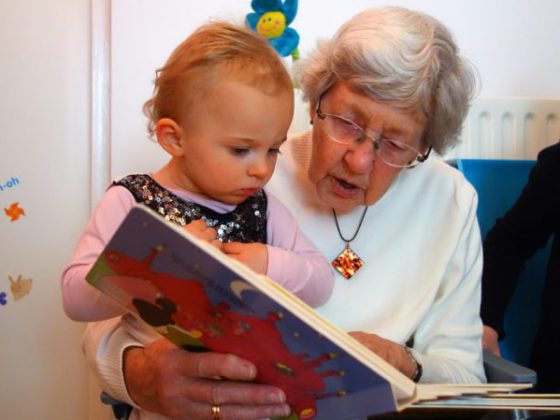 Eine ältere Frau hat ein Kleinkind auf dem Arm und schaut sich ein Buch an.