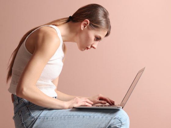 Frau mit einer krummen Haltung sitzt vor einem Laptop